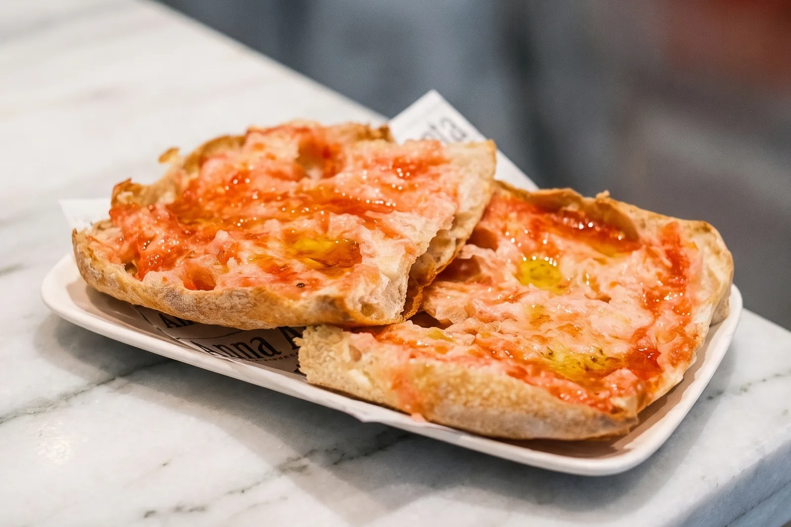 Dos rebanadas de pan con tomate y aceite de oliva, en un plato blanco sobre el mármol.