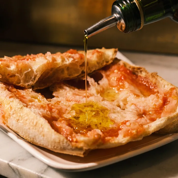 Olive oil being poured over the pan con tomate on a white dish.